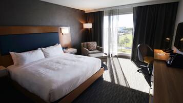 Une chambre d’hôtel avec un grand lit, un bureau, une chaise, une lampe et une vue sur l’extérieur.