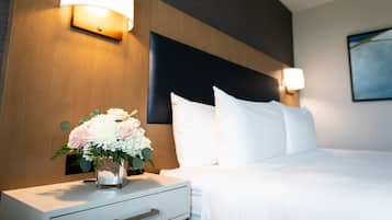 A hotel room with a neatly made bed, a bedside table with a vase of flowers, and wall-mounted lamps.