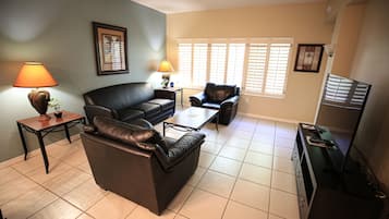 Una sala de estar con sofá, sillón, mesa de centro, lámpara y televisor.