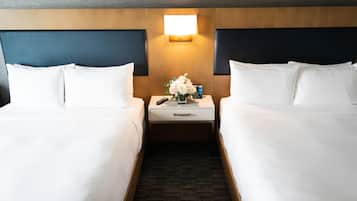 A hotel room with two beds, a nightstand with a lamp, and a small table with a vase of flowers.
