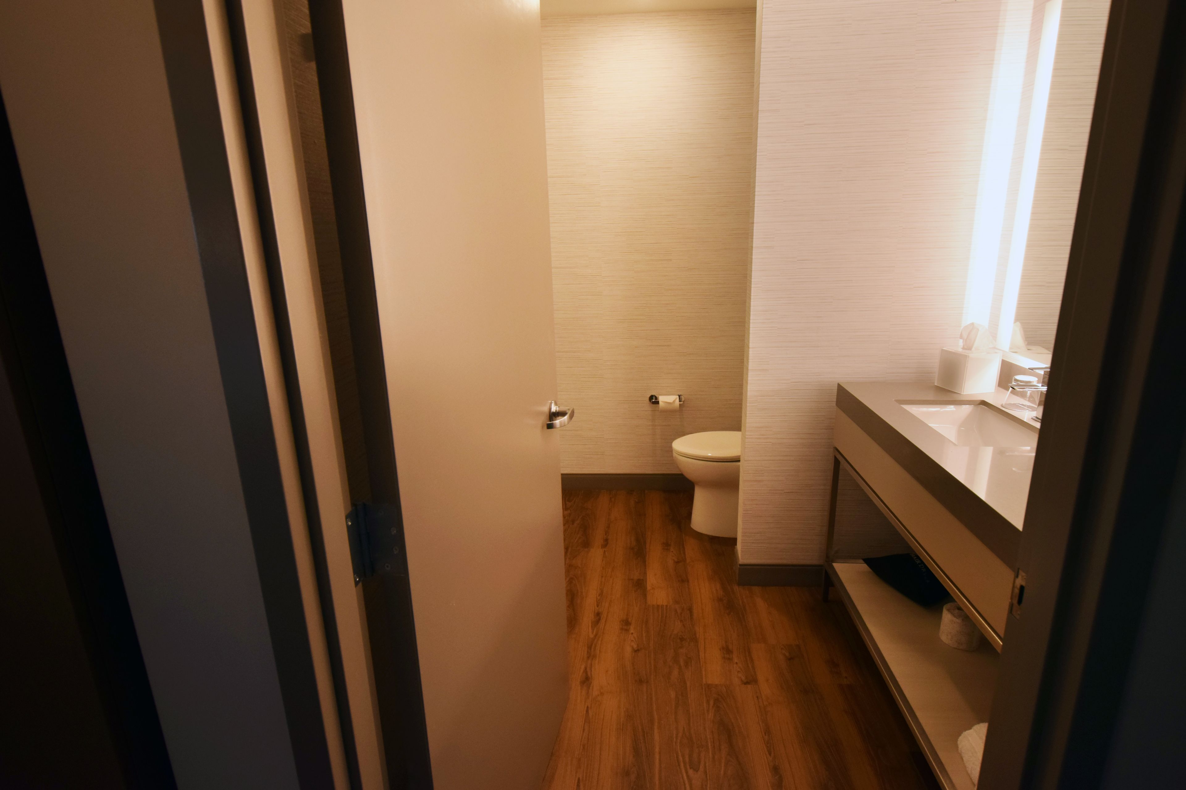 Une petite salle de bain avec un plancher en bois, des toilettes blanches et un meuble-lavabo avec un miroir.