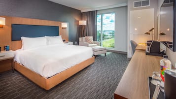 A hotel room with a large bed, a desk with a chair, a lamp, and a view of the outdoors.