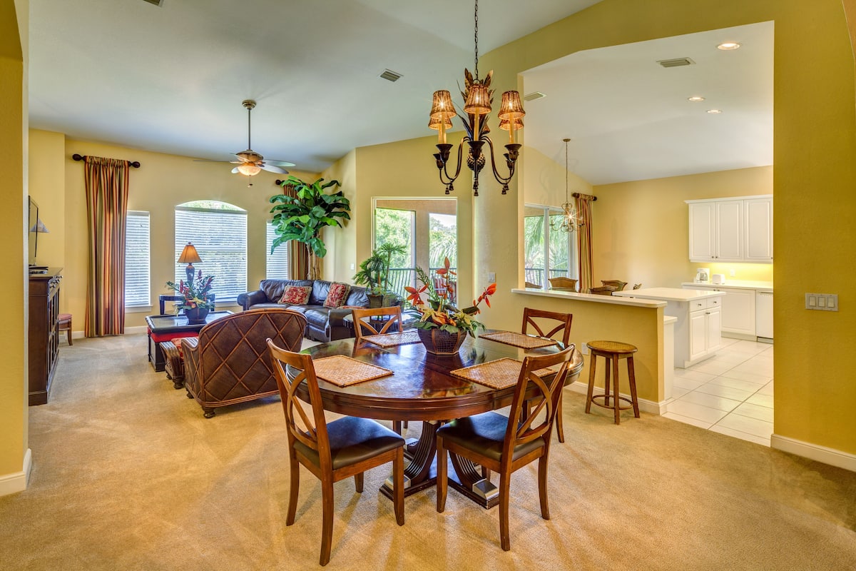 A spacious living room with a round dining table, comfortable seating, and a kitchen area with white cabinets.