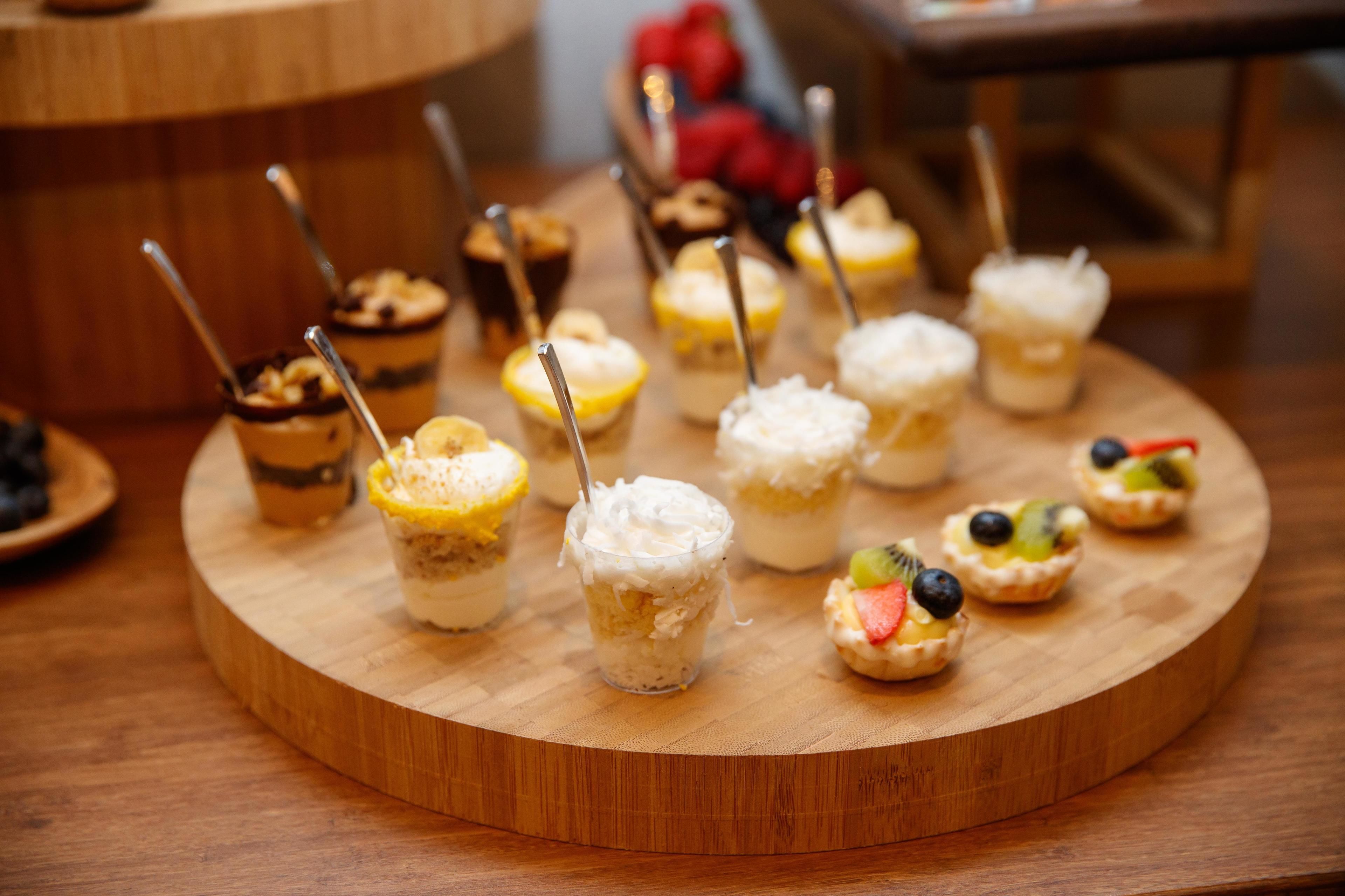 A variety of desserts on a wooden board, including cupcakes with toppings and a small glass with a creamy dessert.