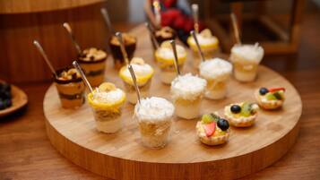 A variety of desserts on a wooden board, including cupcakes with toppings and a small glass with a creamy dessert.