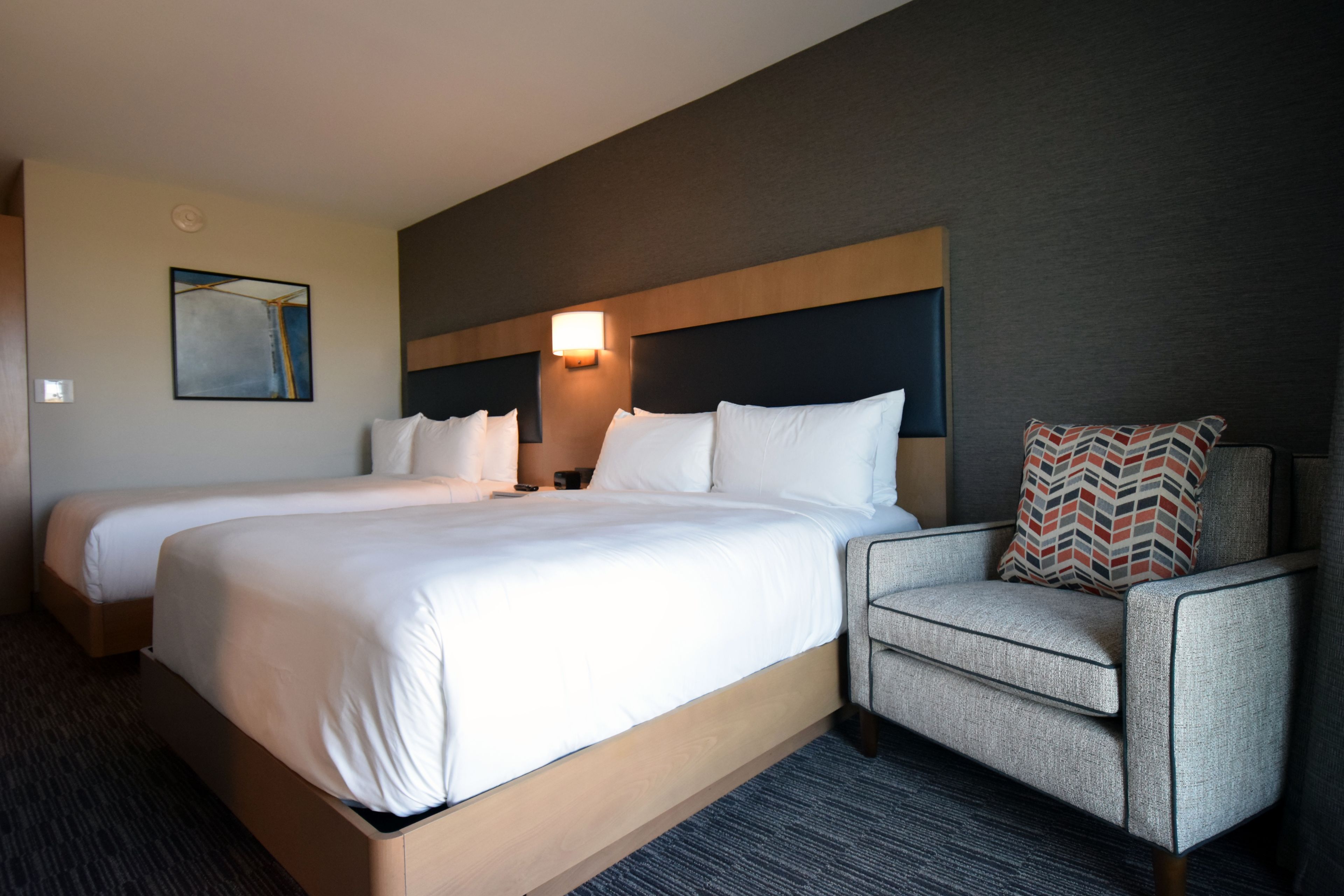 A hotel room with two beds, a sofa, a wall-mounted lamp, and a framed picture.