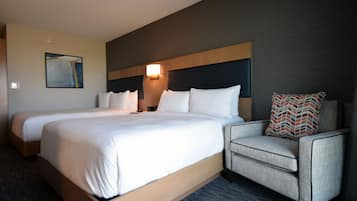 A hotel room with two beds, a sofa, a wall-mounted lamp, and a framed picture.