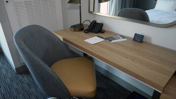 Une chambre d’hôtel avec un bureau en bois, un téléphone, une lampe, une chaise et un lit doté d’une tête de lit.