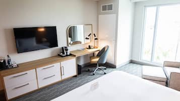 A hotel room with a bed, a desk with a chair, a TV, a mirror, and a wardrobe.