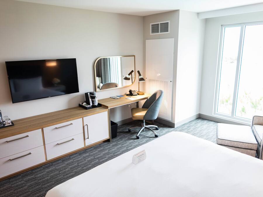 A hotel room with a bed, a desk with a chair, a TV, a mirror, and a wardrobe.