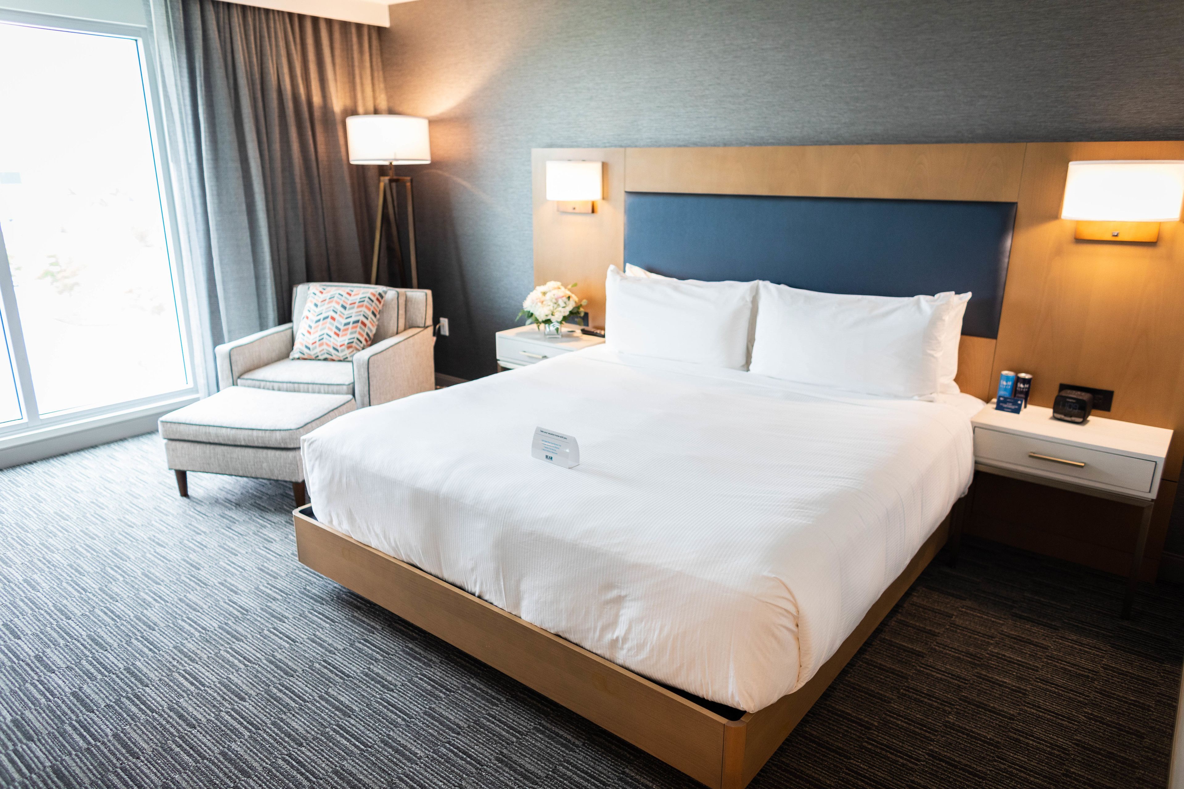 A hotel room with a large bed, a chair, a nightstand, and a lamp.