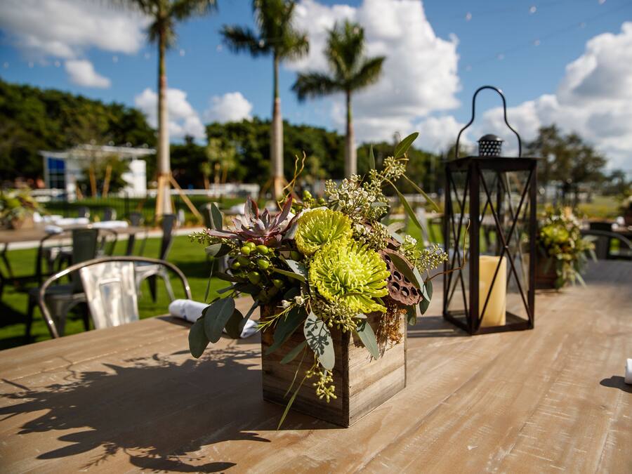 Una mesa de madera con un centro de mesa floral, un farolillo y una servilleta.
