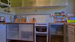 A kitchen with a microwave, stove, oven, and a dishwasher. There are cabinets, a sink, and various kitchen utensils. - Steading Holidays - Comraich (Acharacle)