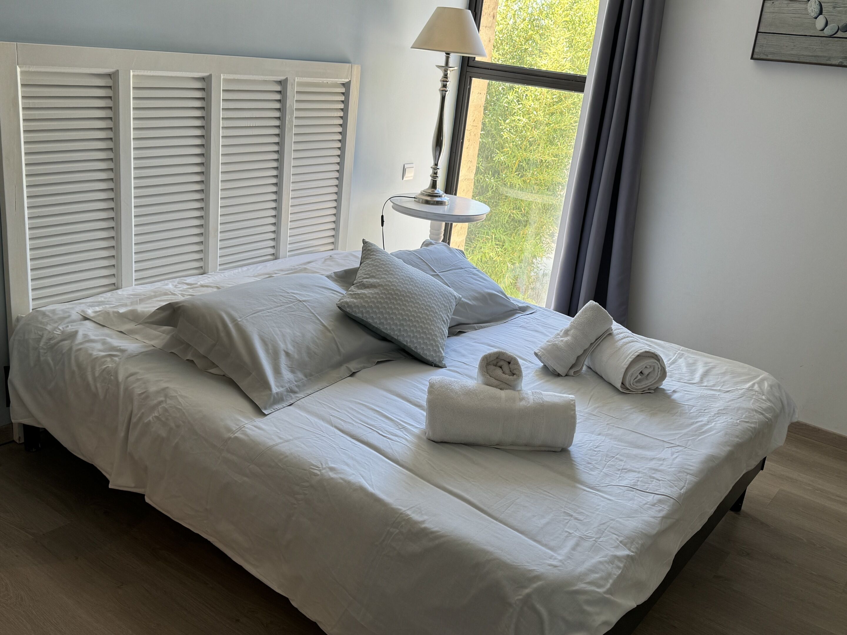 Un letto rifatto con lenzuola e cuscini bianchi, una lampada da comodino e una finestra con tende.