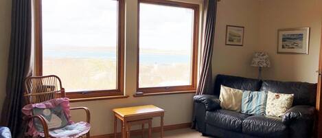 Una sala de estar con vista a la playa, un sofá de cuero, una silla de madera, una mesita y una lámpara.