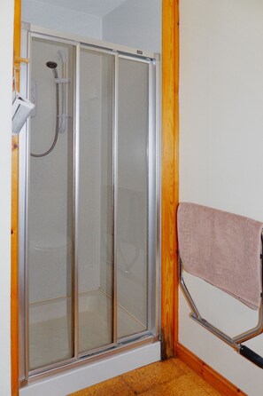Ducha con paredes de vidrio, un cabezal de ducha manual y un perchero con una toalla.