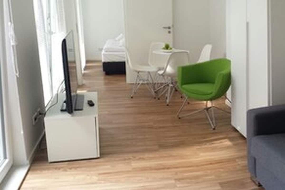Uma sala de estar moderna com um sofá cinza, uma poltrona verde e uma pequena mesa com uma planta.
