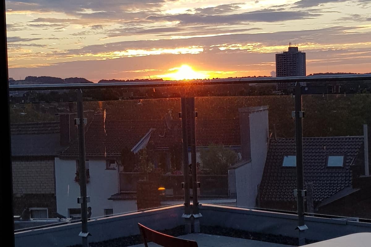 Terraço no telhado com vista para o pôr do sol sobre a paisagem urbana.