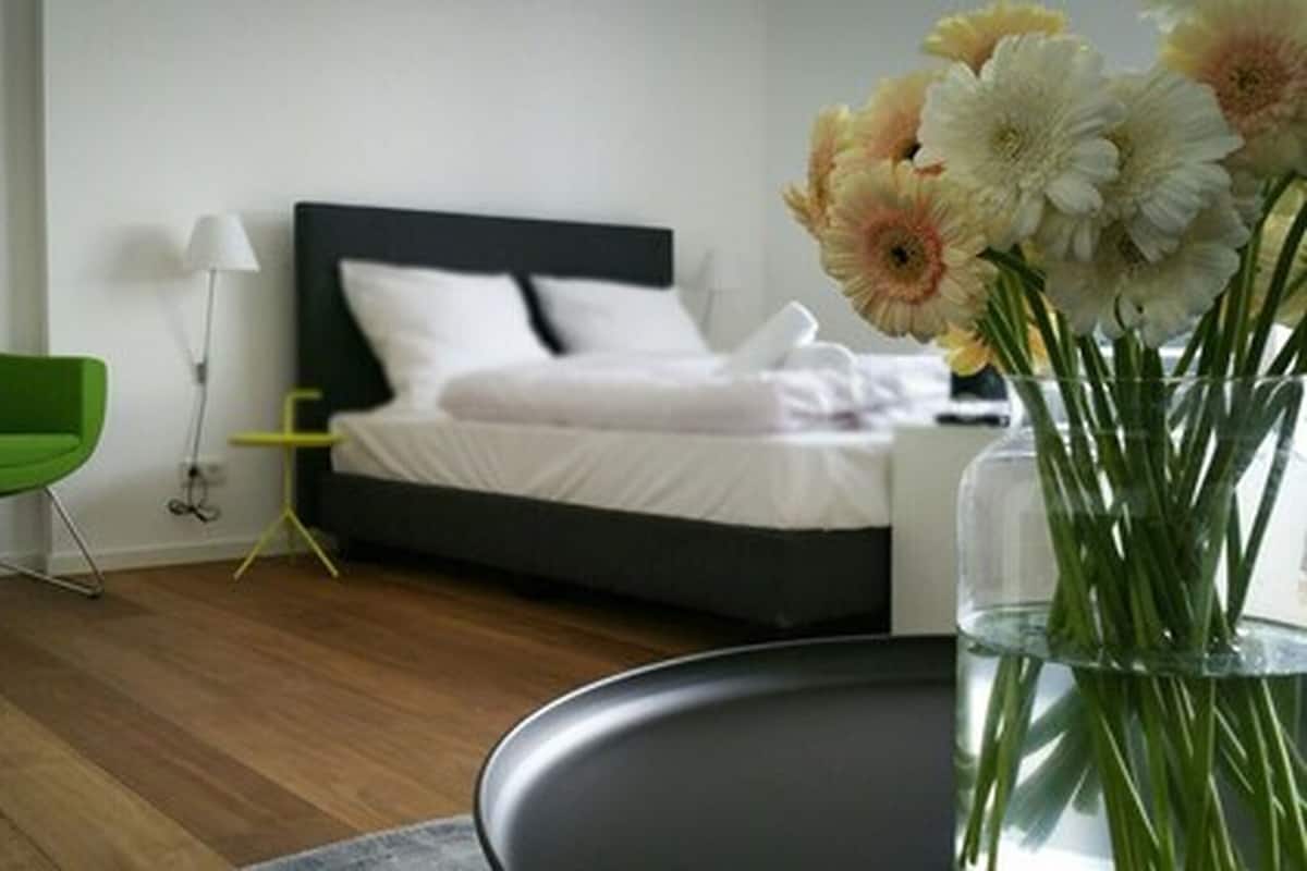 Quarto moderno com cama, uma poltrona verde e um vaso com flores.