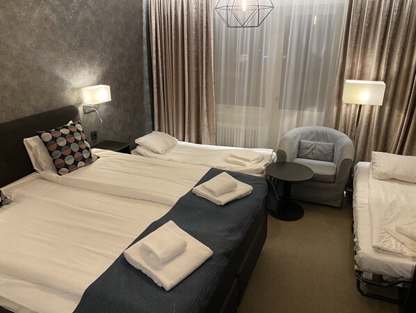 Habitación de hotel con dos camas, una silla y una mesita.