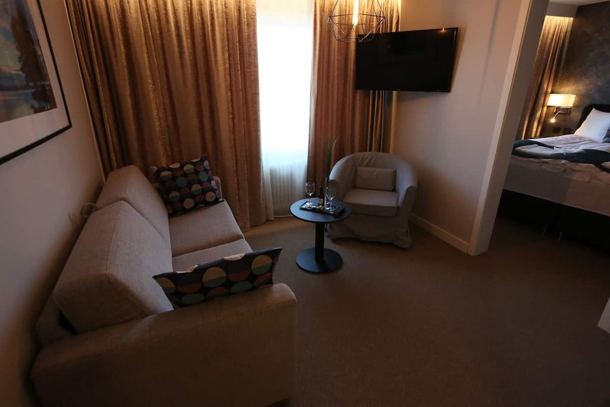 Una habitación de hotel con sofá, sillón, una mesita redonda y una cama.