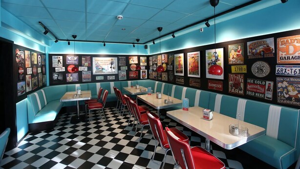 A diner with checkered flooring, teal booths, red chairs, and vintage posters on the walls. - Hotell Rättvik (Rattvik)