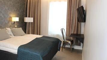 Habitación de hotel con cama, escritorio, silla, televisor y ventana con cortinas.