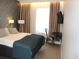 A hotel room with a bed, a desk, a chair, a TV, and a window with curtains.