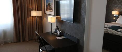 A hotel room with a desk, chair, and a bed.