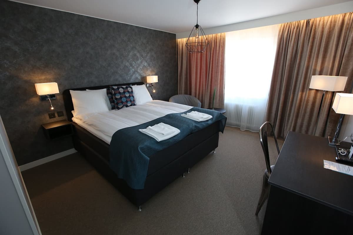 Una habitación de hotel con una cama grande, dos mesitas de noche con lámparas, un escritorio y una silla.