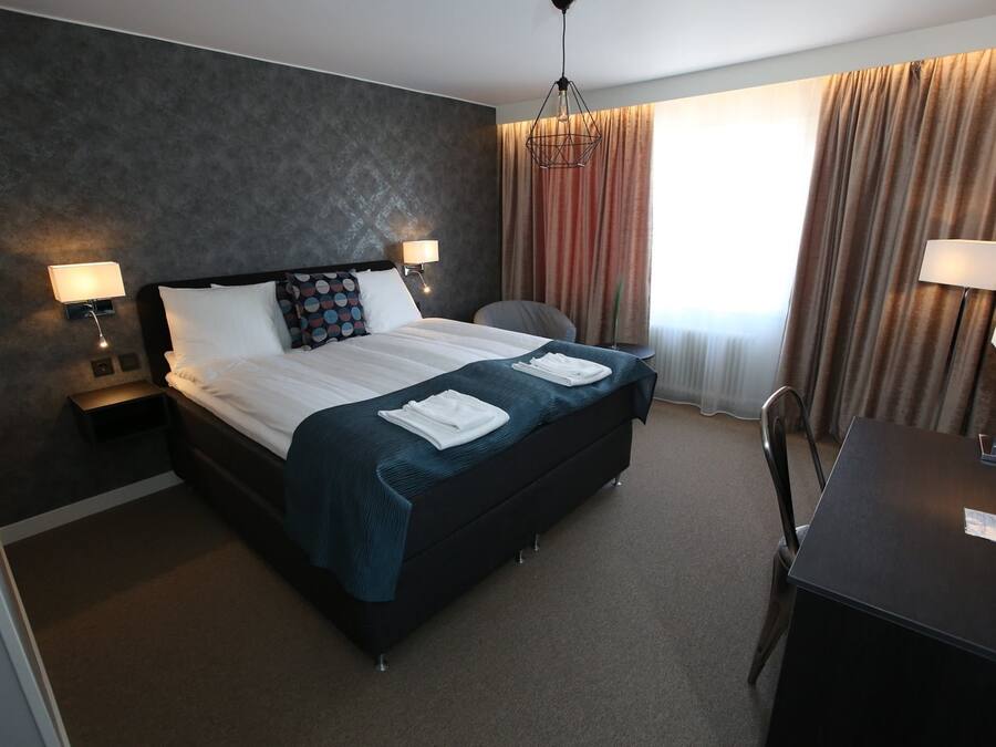 Una habitación de hotel con una cama grande, dos mesitas de noche con lámparas, un escritorio y una silla.