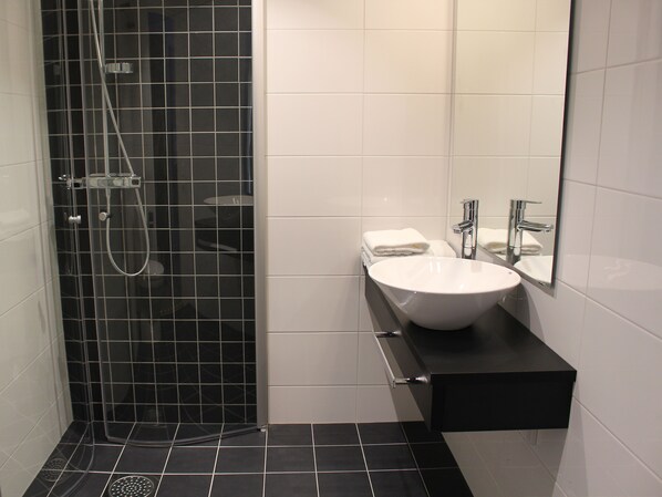 Un baño moderno con ducha de azulejos negros, un lavamanos blanco con espejo y encimera negra.