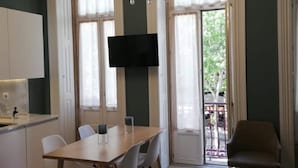 A modern kitchen with a dining area, a flat-screen TV mounted on the wall, and a large window with a view of greenery outside. - Mercado dos Poetas (Porto)