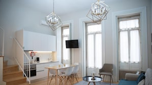A modern apartment with a kitchen, dining area, and living room. It includes a staircase, a TV, and large windows. - Mercado dos Poetas (Porto)