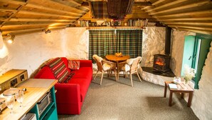 Ein gemütliches Dachzimmer mit einem roten Sofa, Korbstühlen, einem kleinen Tisch, einem Herd und einem Bücherregal.