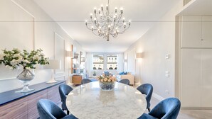 Et moderne spiseområde med et rundt marmorbord, blå polstrede stole og en lysekrone.