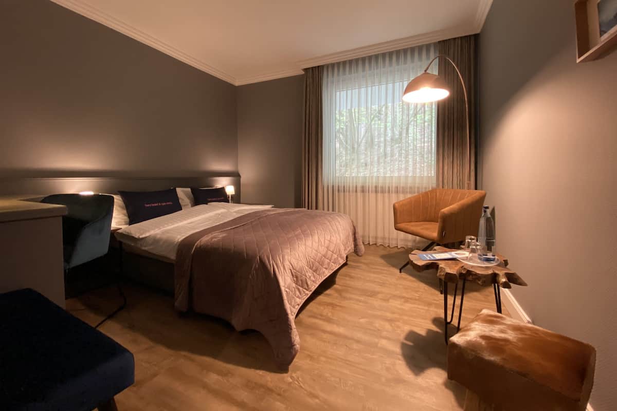 A hotel room with a bed, a desk, a chair, a small table, and a window with curtains.