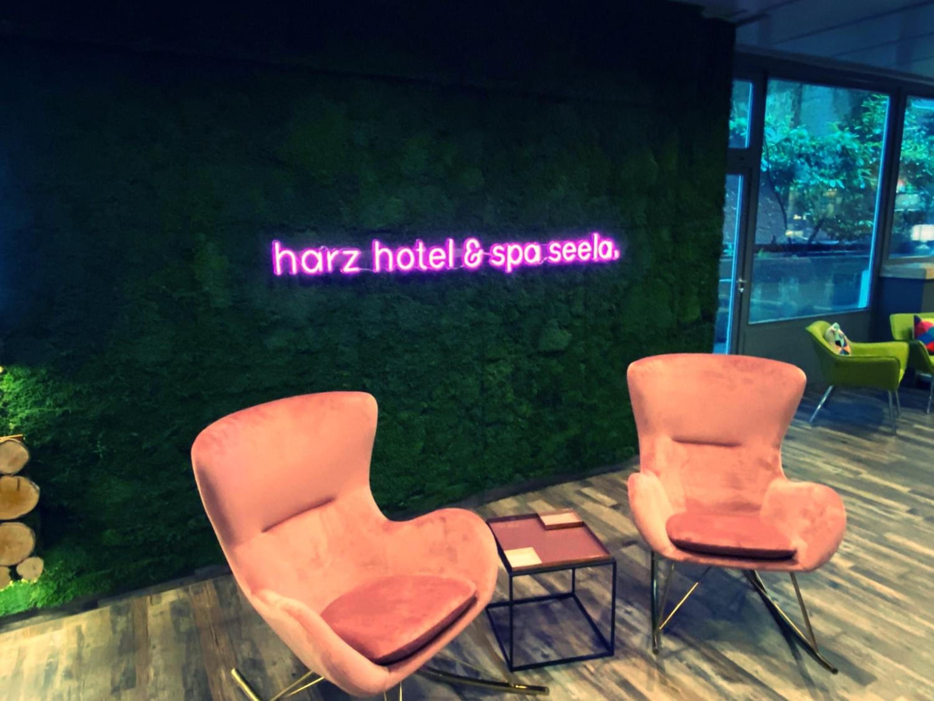 A spa area with a neon sign reading 'harz hotel & spa seela.' There are two pink chairs and a small table in the foreground.