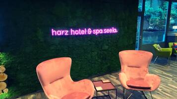 Un área de spa con un letrero de neón que dice 'harz hotel & spa seela'. Hay dos sillones rosados y una mesita pequeña en primer plano.