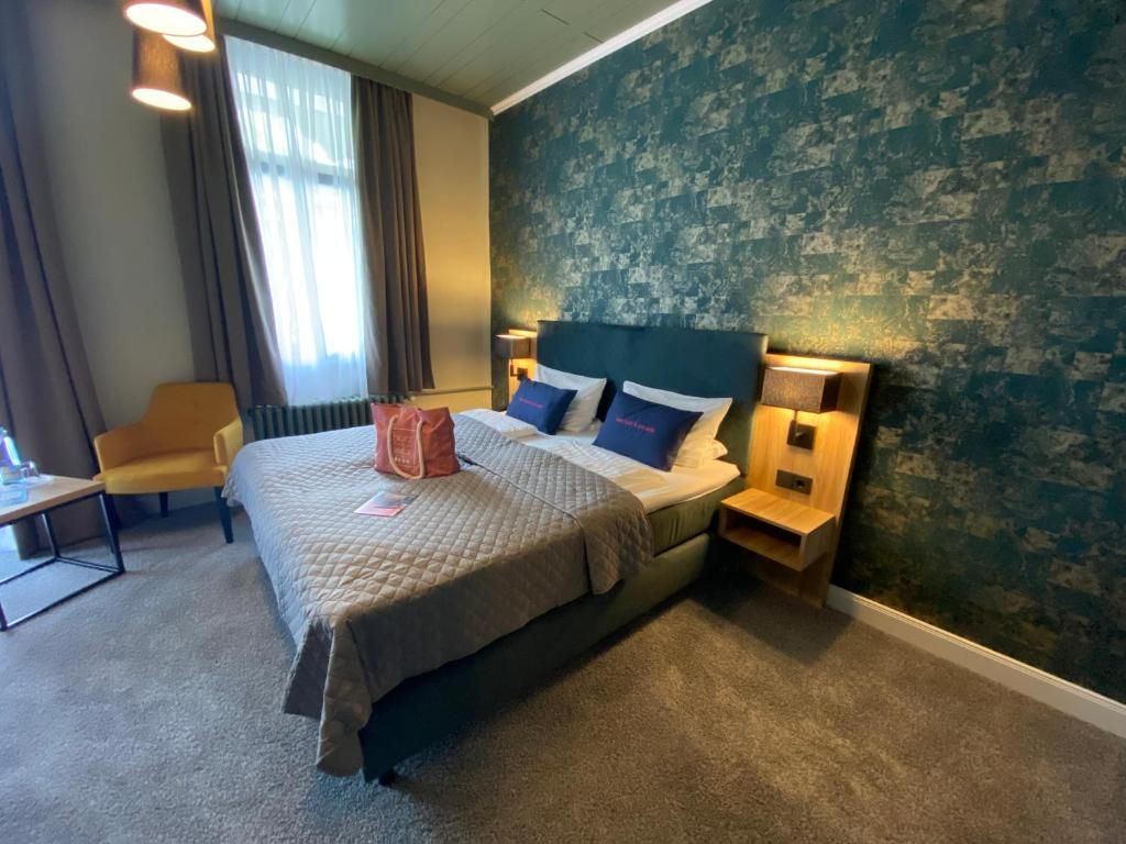 A hotel room with a bed, bedside tables, a chair, and a window with curtains.