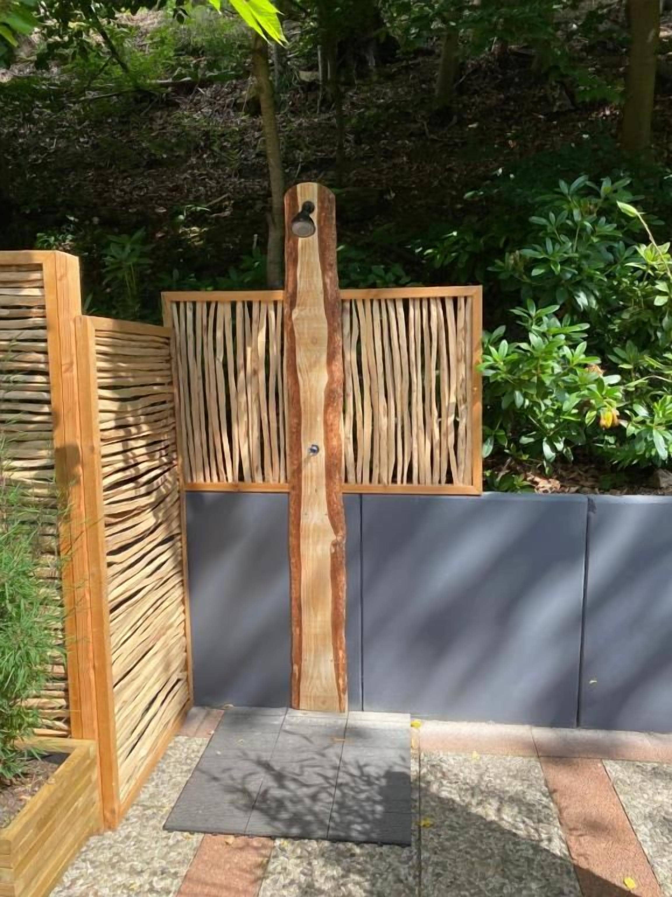 Una verja de madera con listones verticales y un pilar central, que da acceso a un jardín con un sendero de piedra.