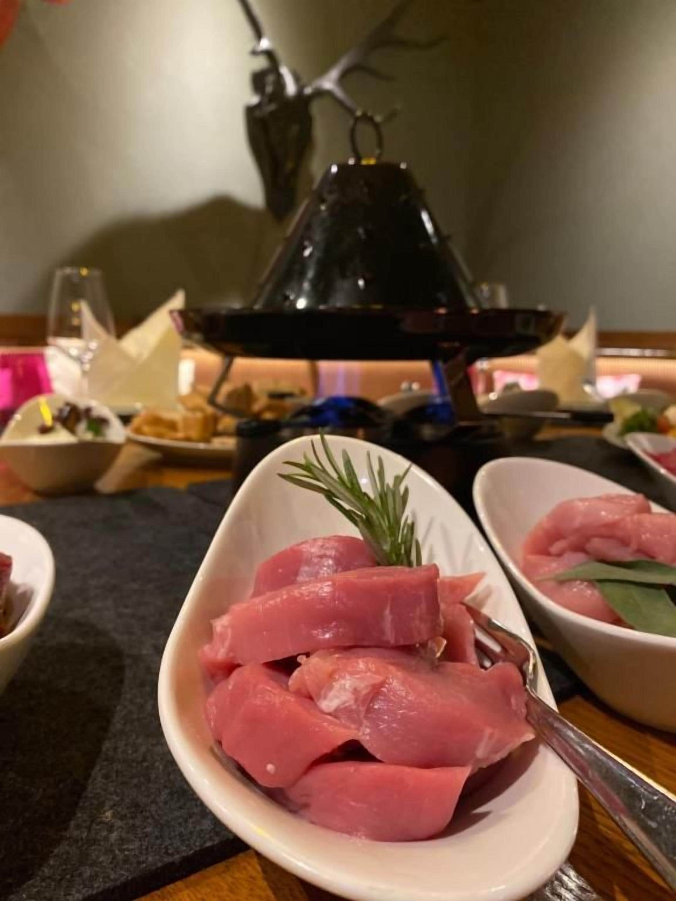 A dining table with a black lamp, a white plate with raw meat, and a sprig of rosemary.