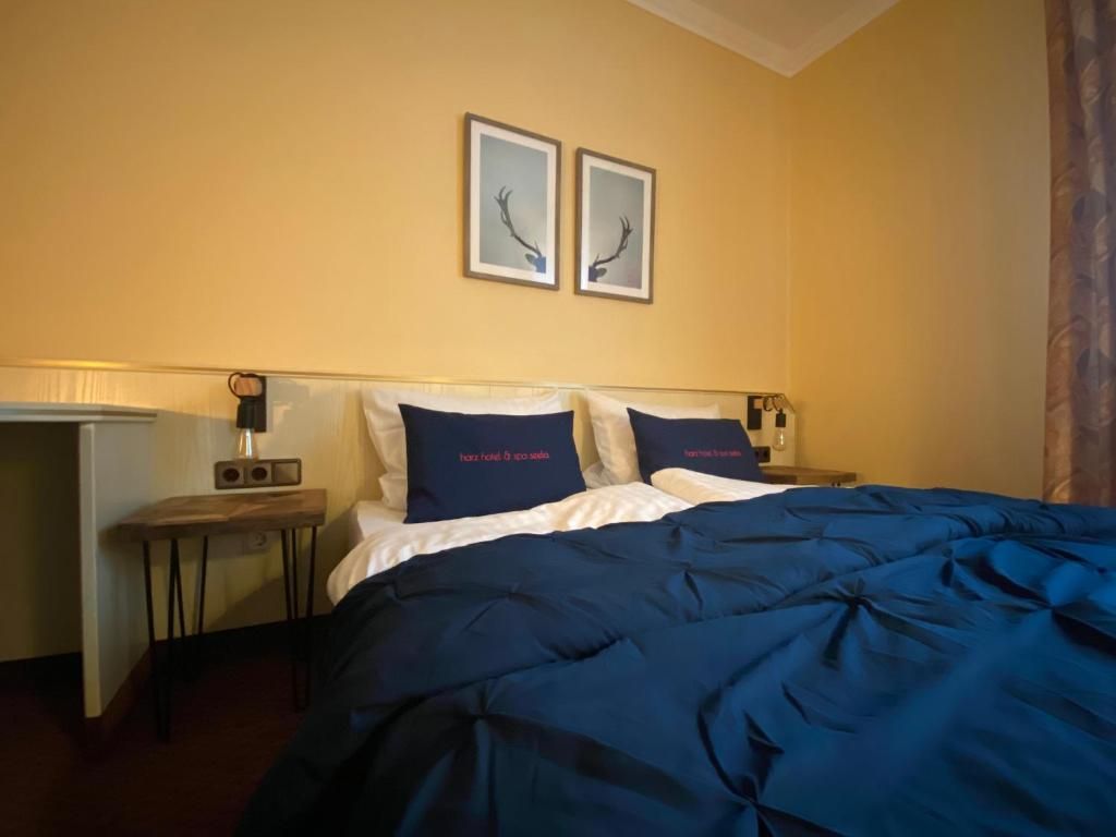 A hotel room with a bed, two bedside tables, a nightstand, and two framed pictures on the wall.