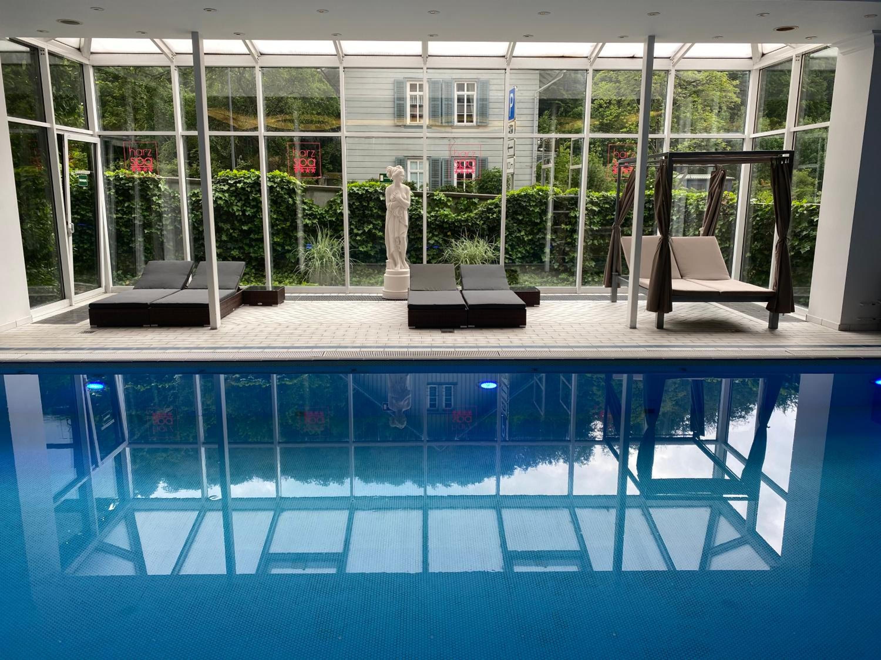 A swimming pool with lounge chairs and a statue, surrounded by glass walls and greenery.