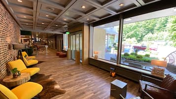Um hall moderno com parede de tijolos, cadeiras amarelas, piso de madeira e amplas janelas com vista para o exterior.