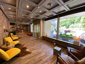 A modern lobby with a brick wall, yellow chairs, a wooden floor, and large windows offering a view of the outdoors. - Harz Hotel & Spa Seela (Bad Harzburg)