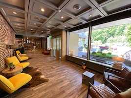 Um hall moderno com parede de tijolos, cadeiras amarelas, piso de madeira e amplas janelas com vista para o exterior.