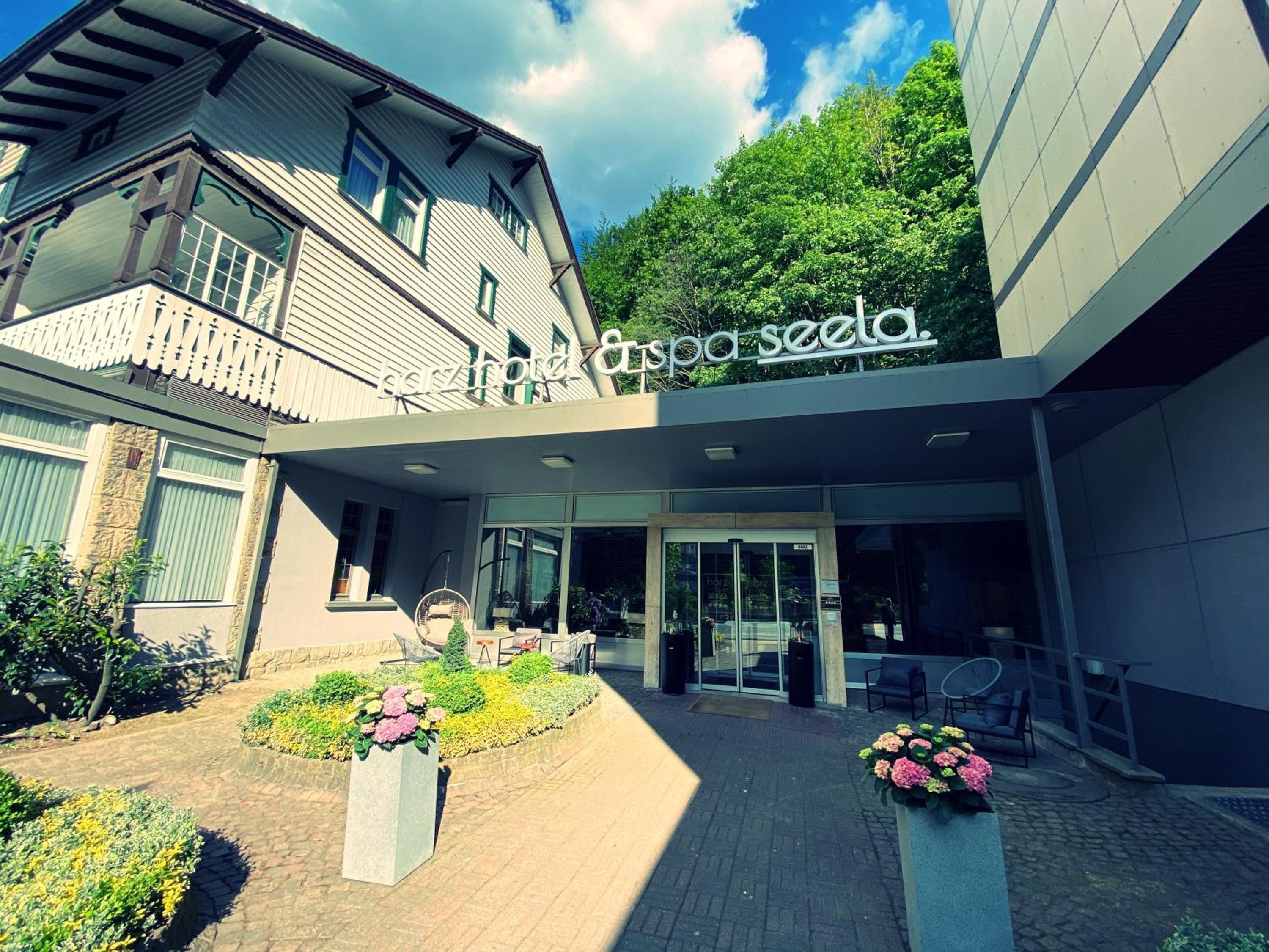A hotel entrance with a modern facade, a covered entrance area, and a landscaped garden with flower beds.