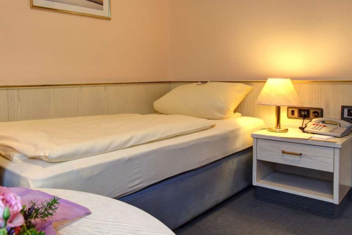 A hotel room with a bed, bedside table with a lamp, and a telephone.