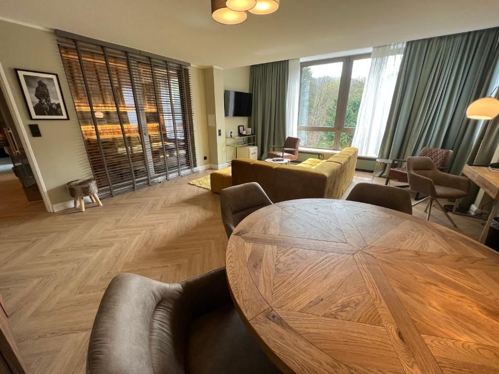 Una sala de estar moderna con una mesa redonda de madera, sofás de cuero, un televisor y un ventanal con cortinas.